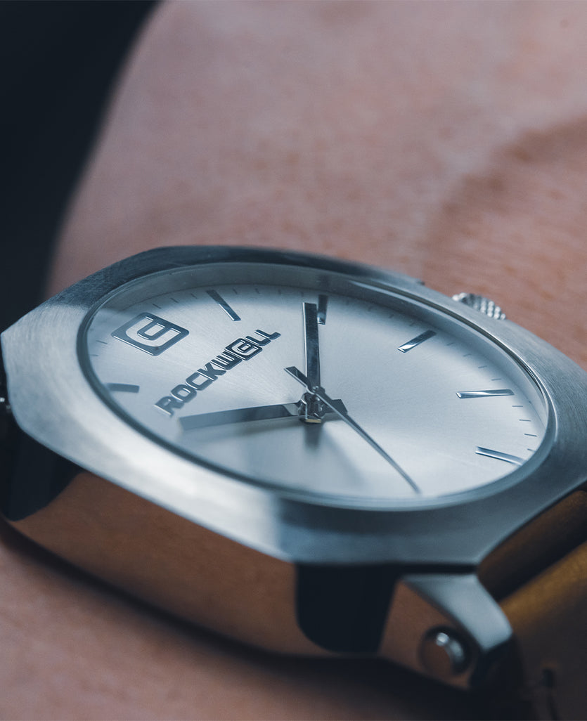 Silver watch on wrist with black strap, Rockwell logo on brushed dial