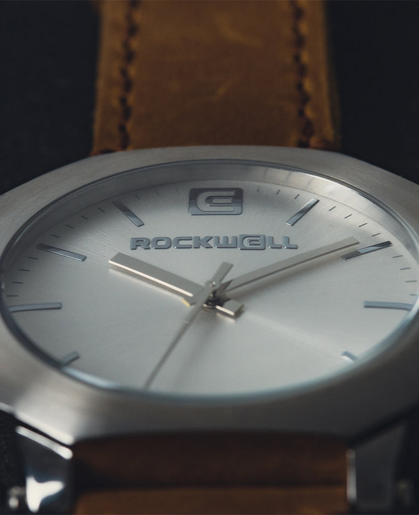 Close-up of silver watch dial with Rockwell logo and tan leather strap