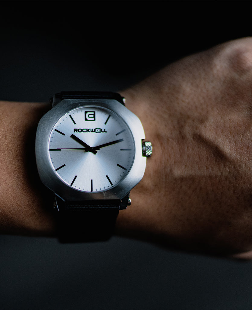 Silver-tone round watch on wrist with black strap and white dial