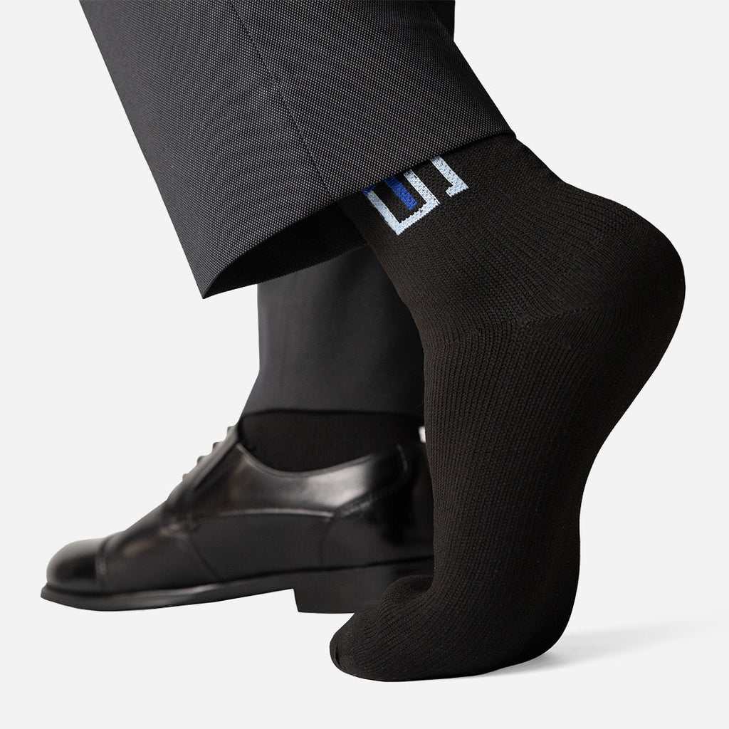 Black crew socks with blue logo patch, worn with a dress shoe