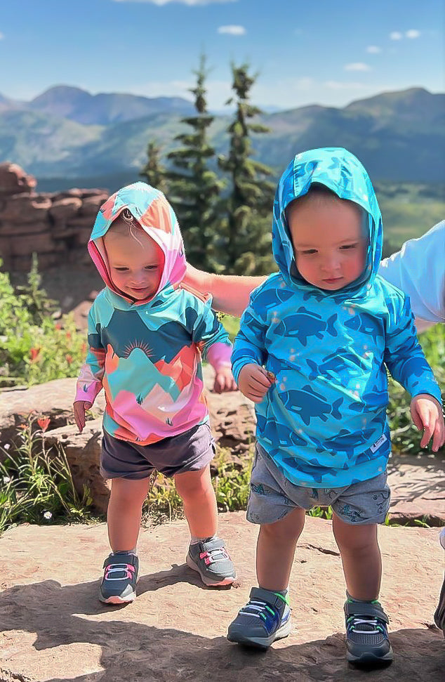 Kids sun hoodie in blue camo print with hood, paired with a pink printed hoodie