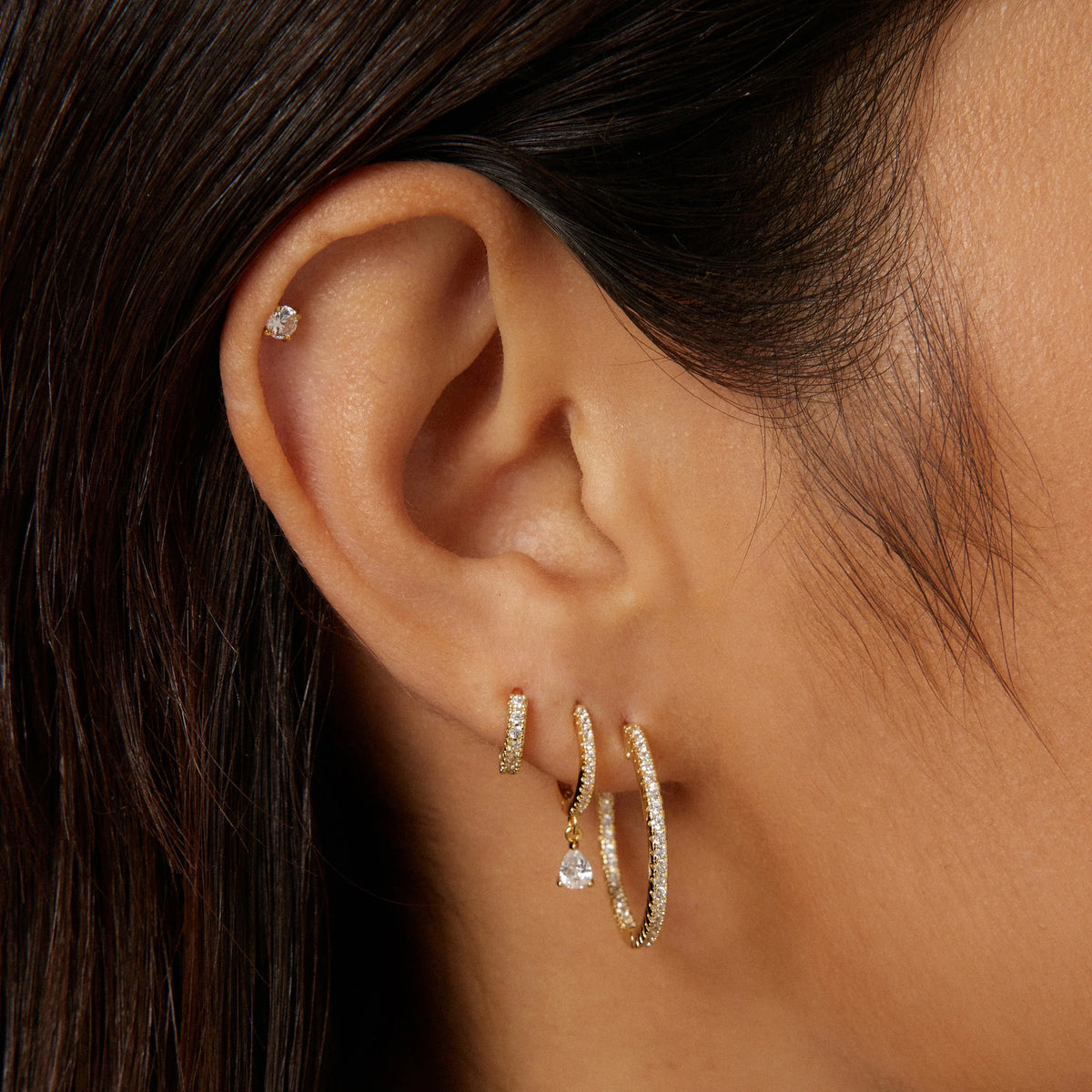 Gold-tone CZ hoop earrings on ear, with pear-drop charm details