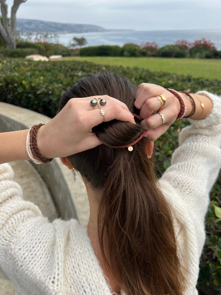 Stacked braided hair tie bracelets on wearer’s wrist with gold-tone charms