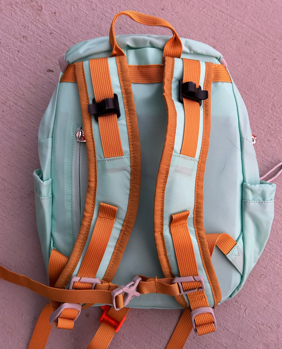 Light blue kids hiking backpack back view with orange padded harness straps