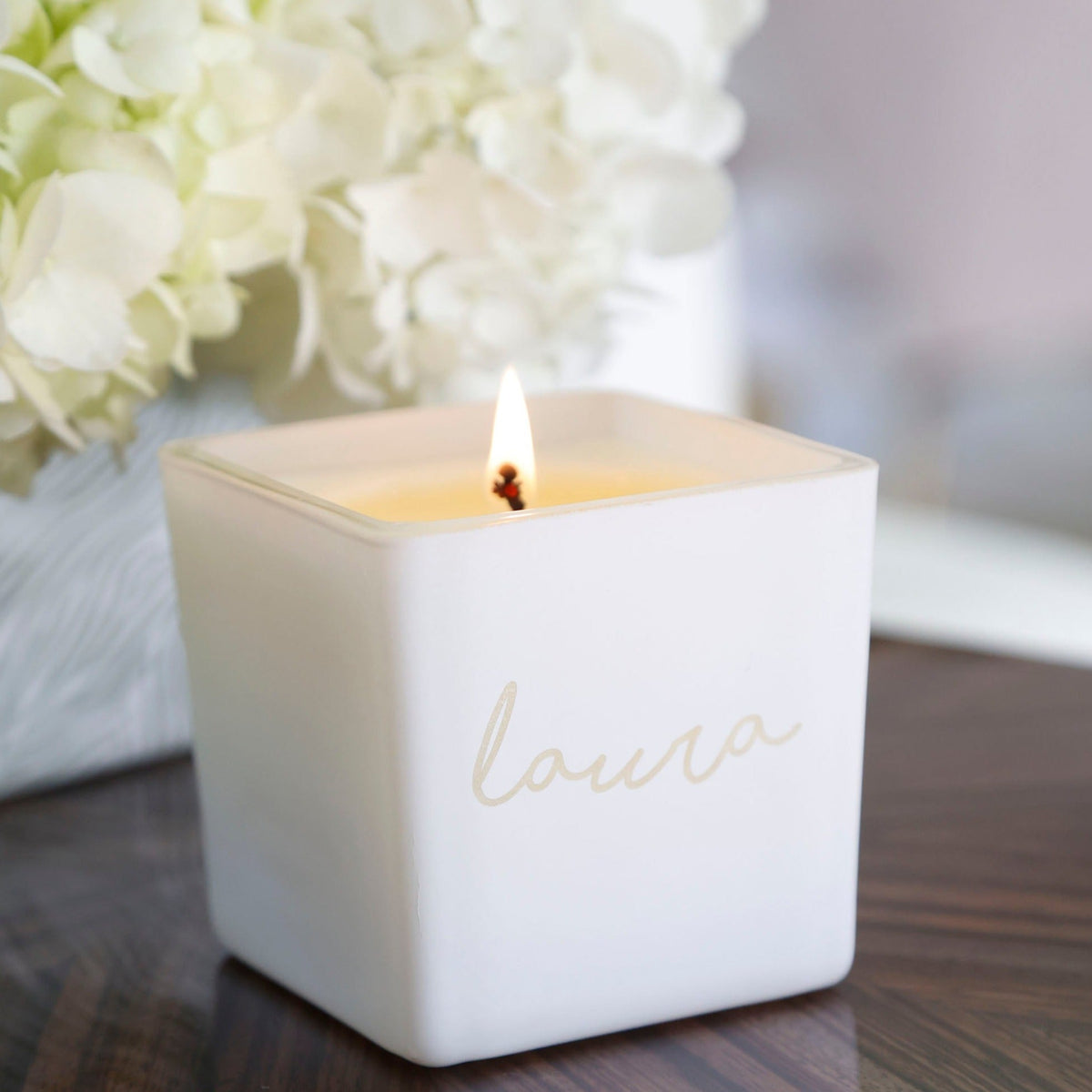 Lit white engraved candle jar with laura name in cursive