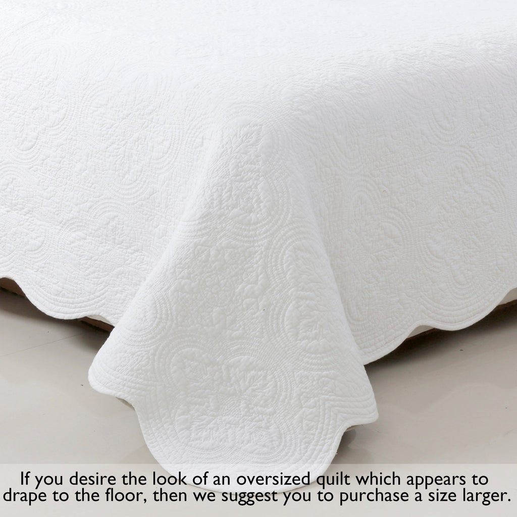 White quilt draped on bed with scalloped hem edge