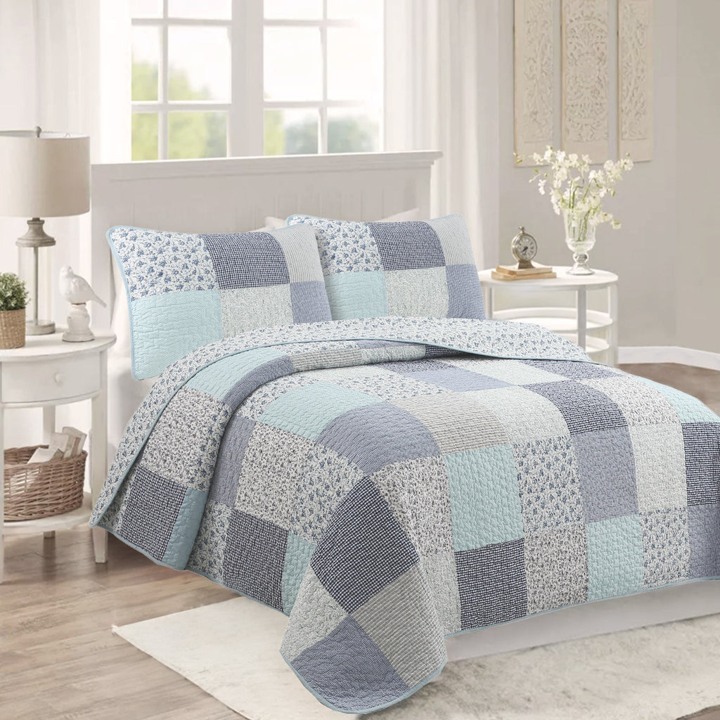 Blue patchwork quilt bedding set with square blocks and floral prints, styled with two shams