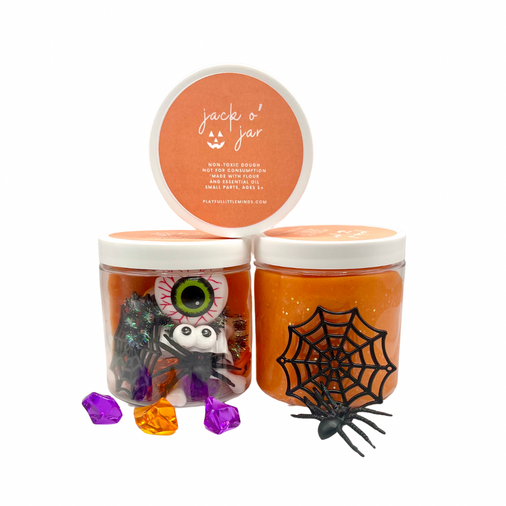 Orange playdough jars with jack-o’-lantern and spider sensory toys, plus purple and orange gems