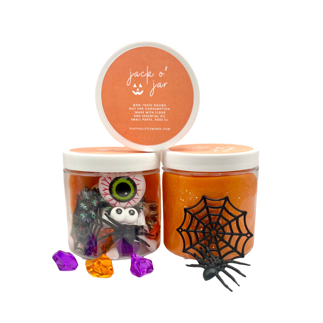 Orange playdough jars with jack-o’-lantern and spider sensory toys, plus purple and orange gems