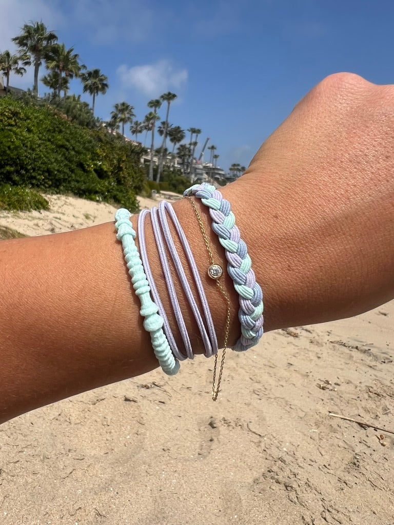 Wrist stack of braided hair tie bracelets, mint and purple tones with gold discs