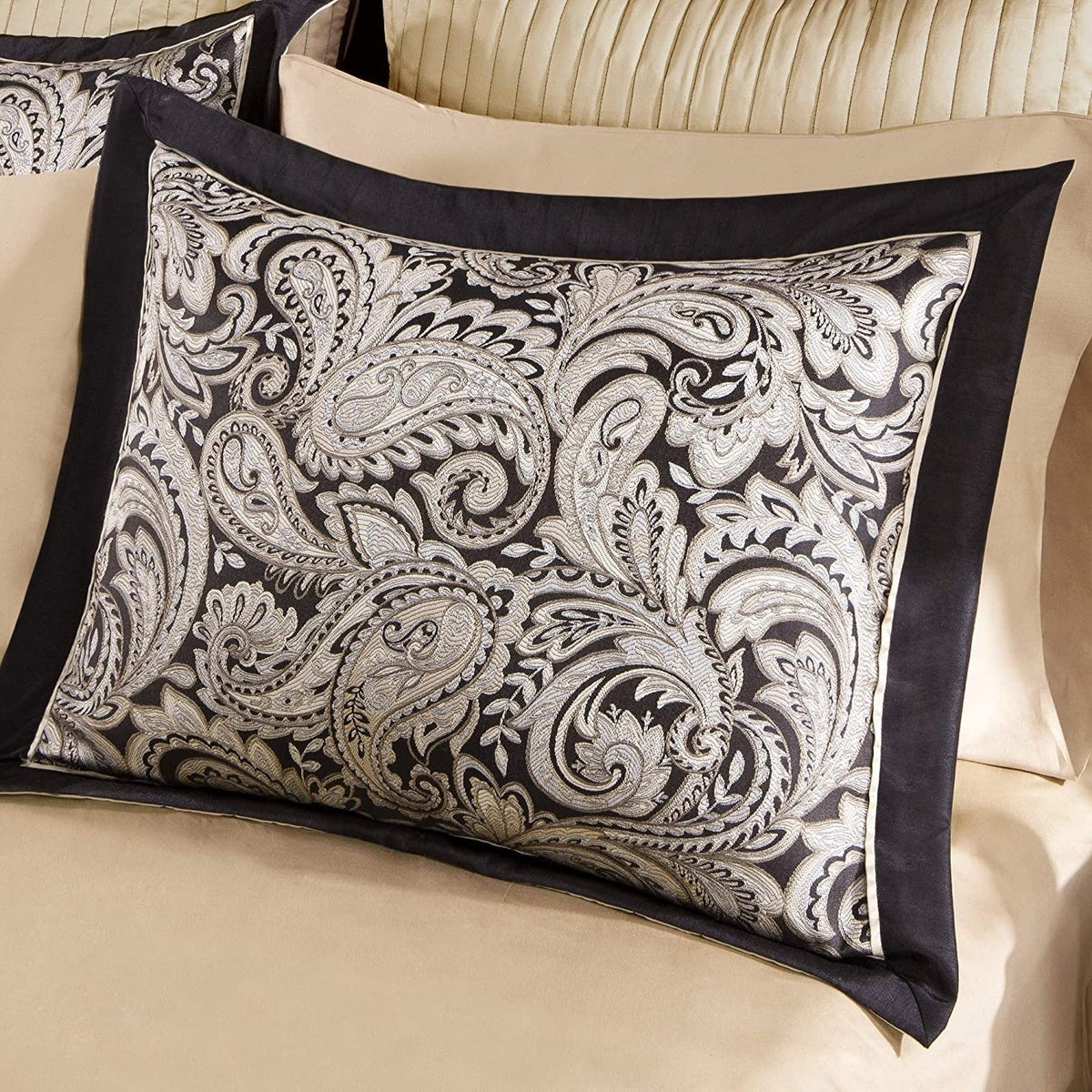 Decorative black-and-white paisley pillow with dark trim on a beige bed