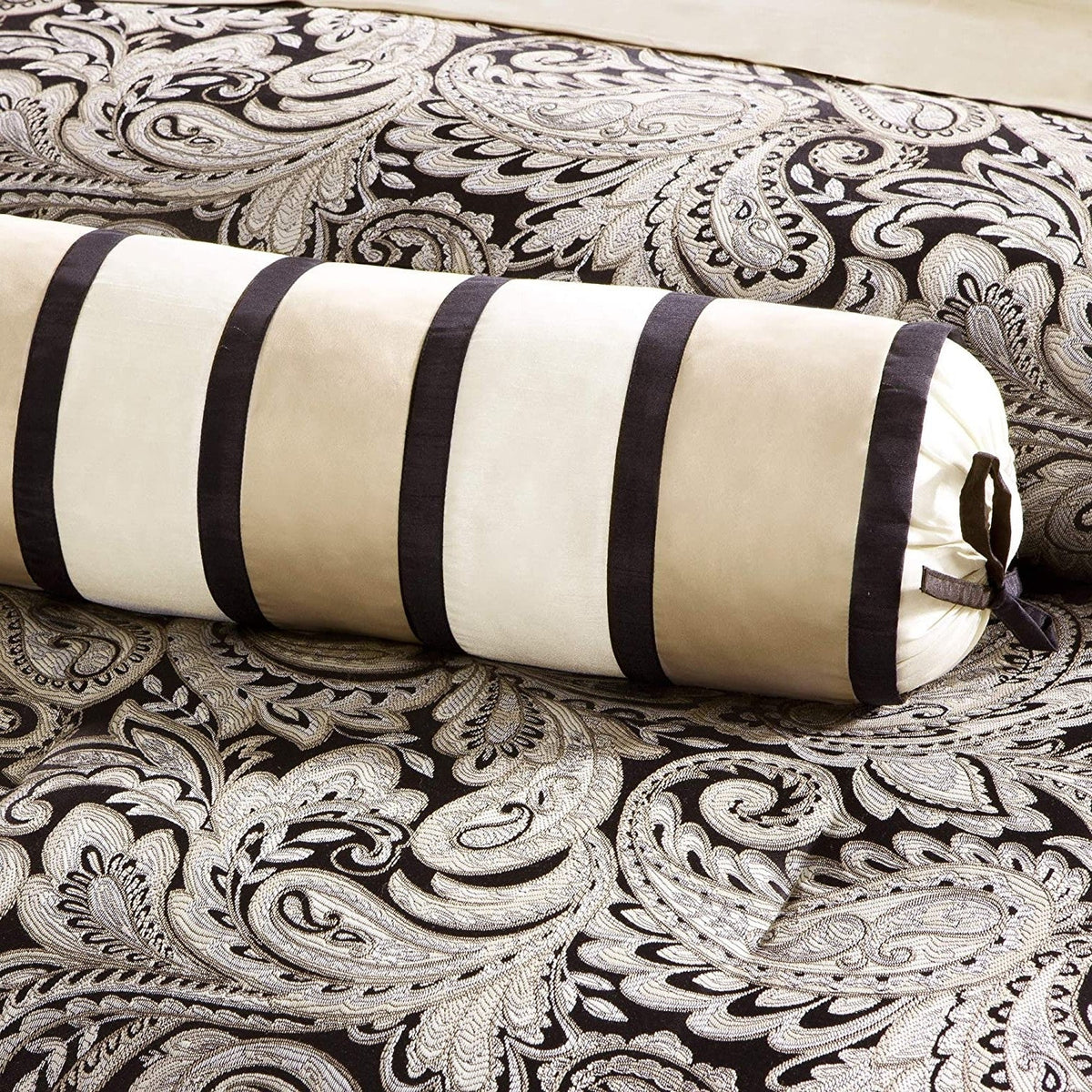 Cream and black striped bolster pillow on black-and-white paisley bedding