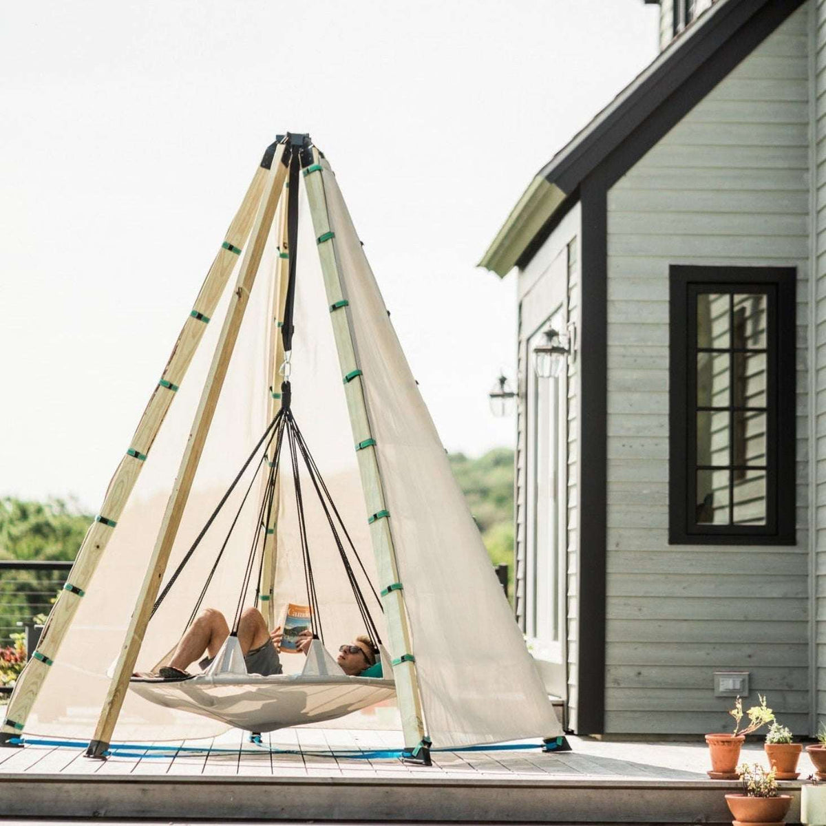 Tipi-style play tent with off-white canvas, wooden poles, green trim and rope supports