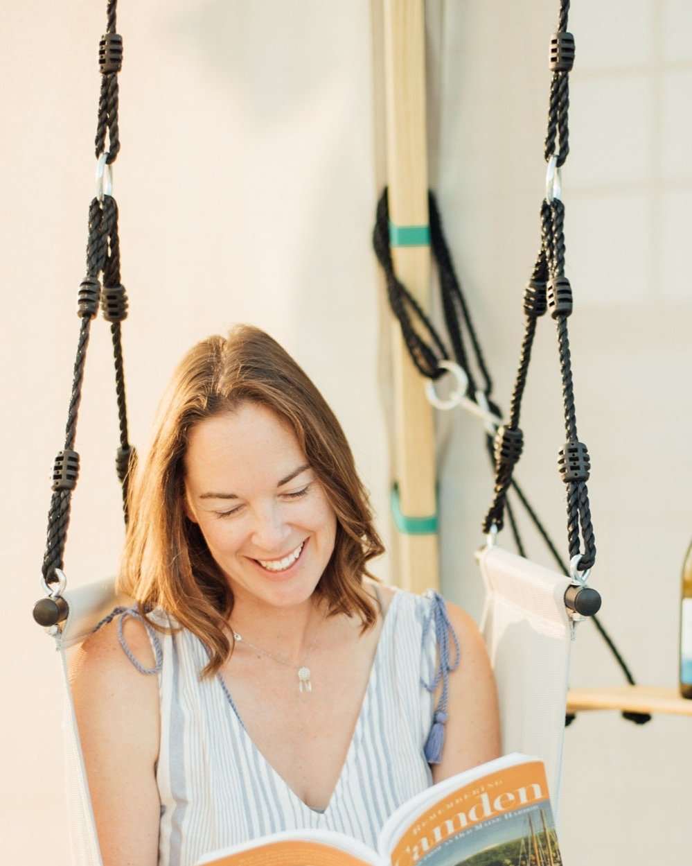 Bijou Rest hanging wooden swing with black ropes, person sitting and reading