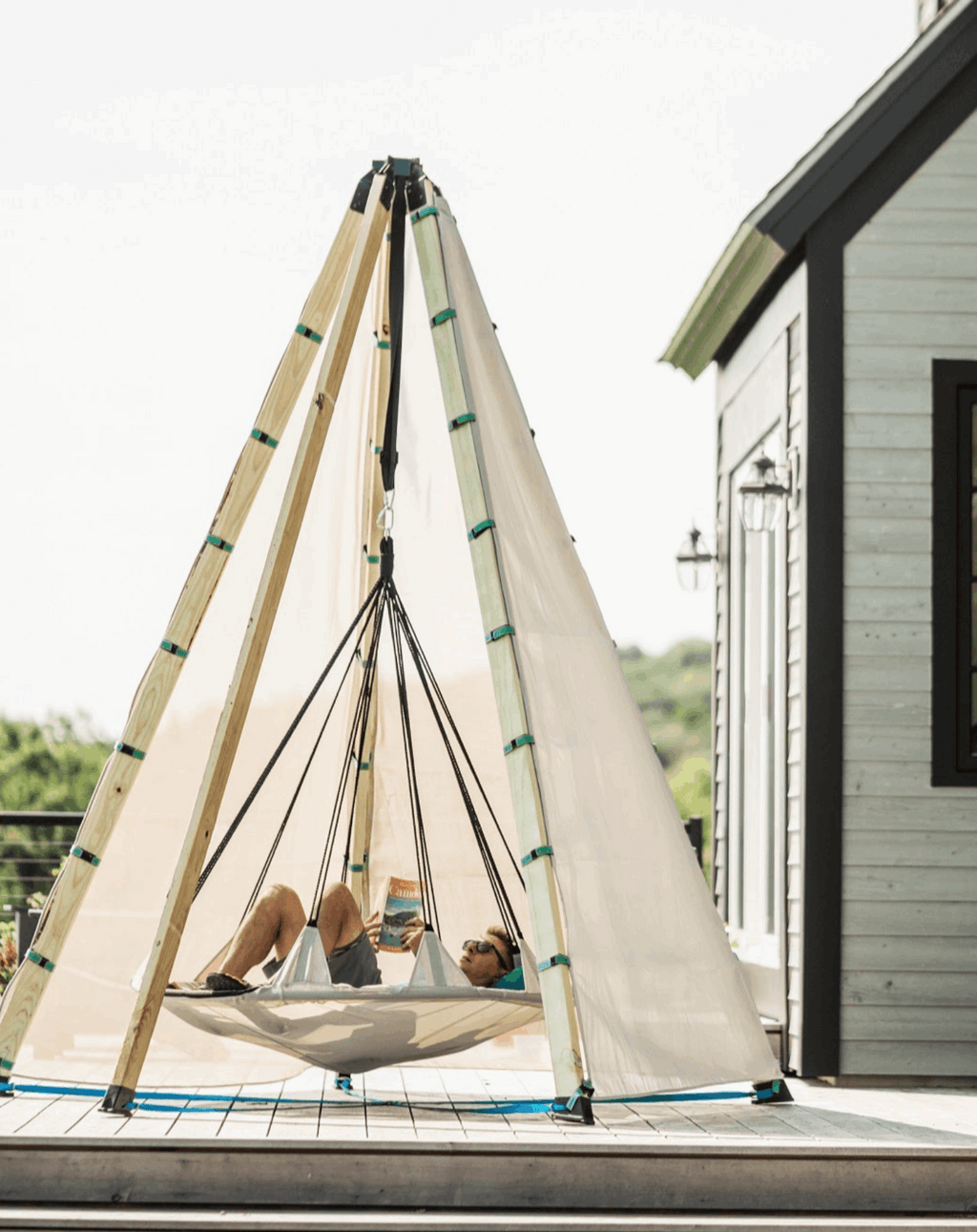 Off-white tipi-style play tent with wooden poles, green trim, and people lying inside
