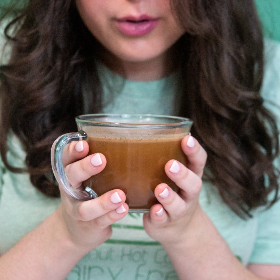 Woman holding a mug of hot cocoa, creamy brown drink in a clear glass cup