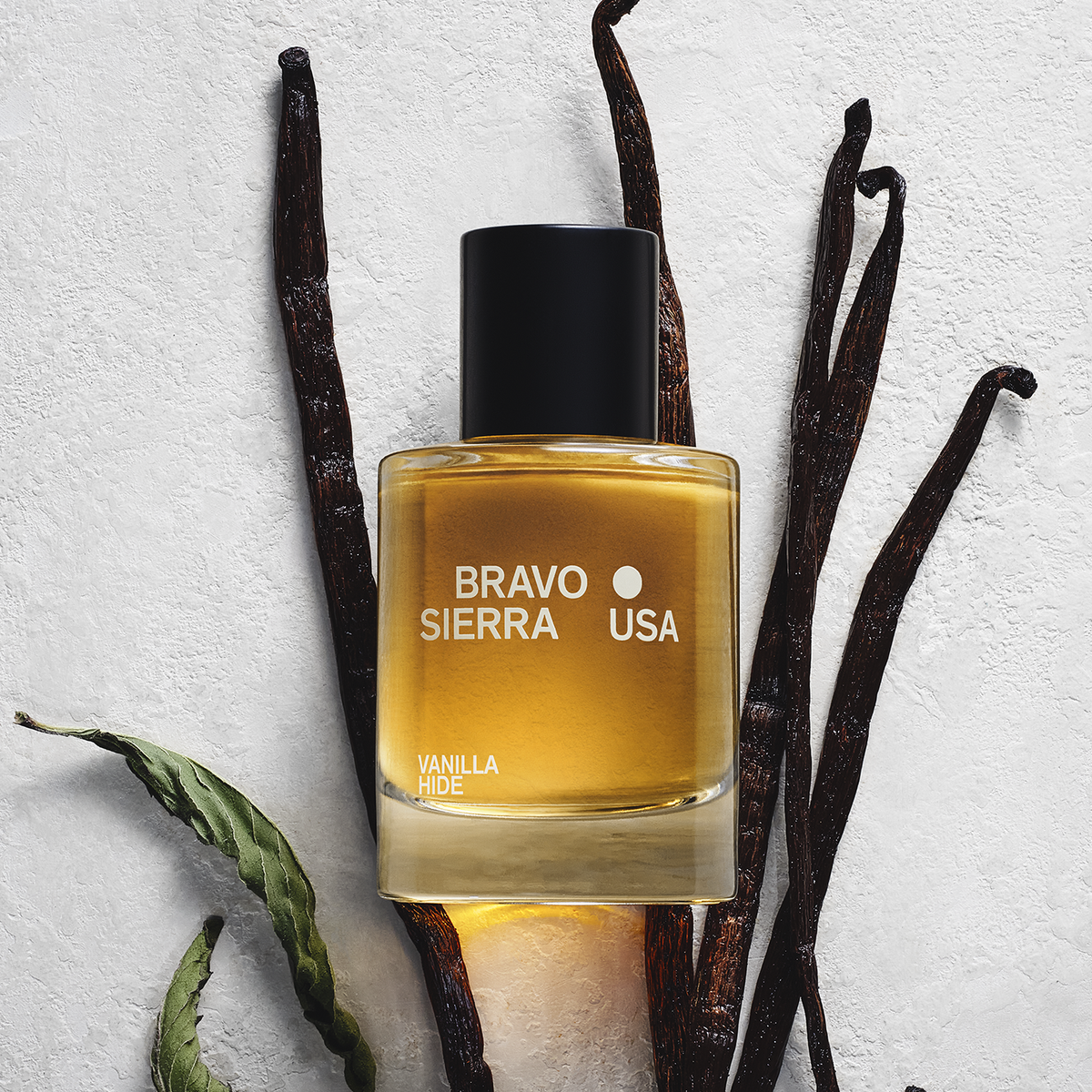 Perfume bottle with black cap and amber liquid, with vanilla pods nearby