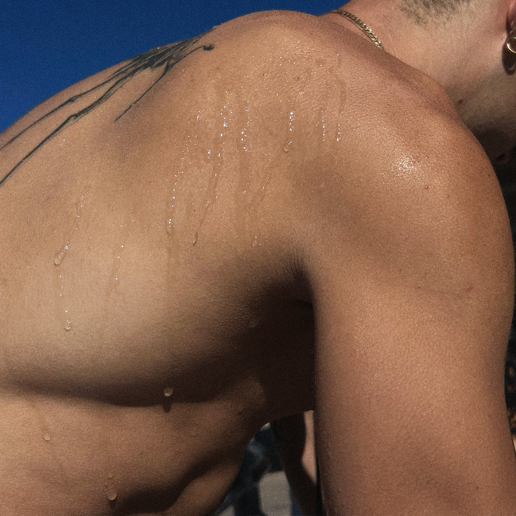 Perfume droplets on bare shoulder skin with subtle shimmer