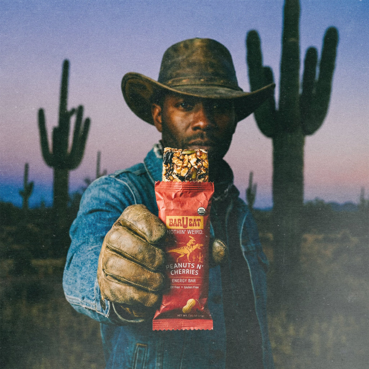 Peanuts N' Cherries energy bar wrapper held in front of a cowboy in a hat