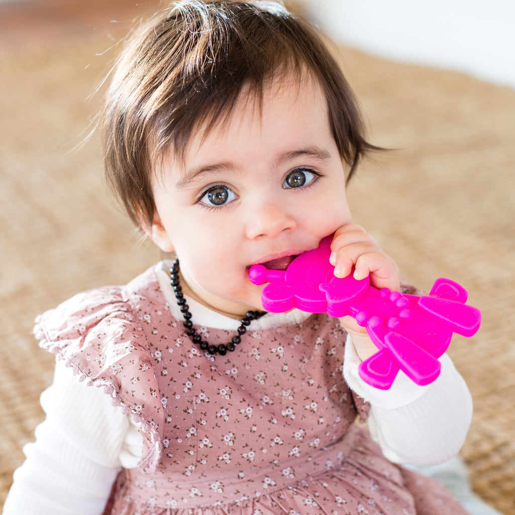 Magenta baby teething toy held by a toddler while chewing the textured tip