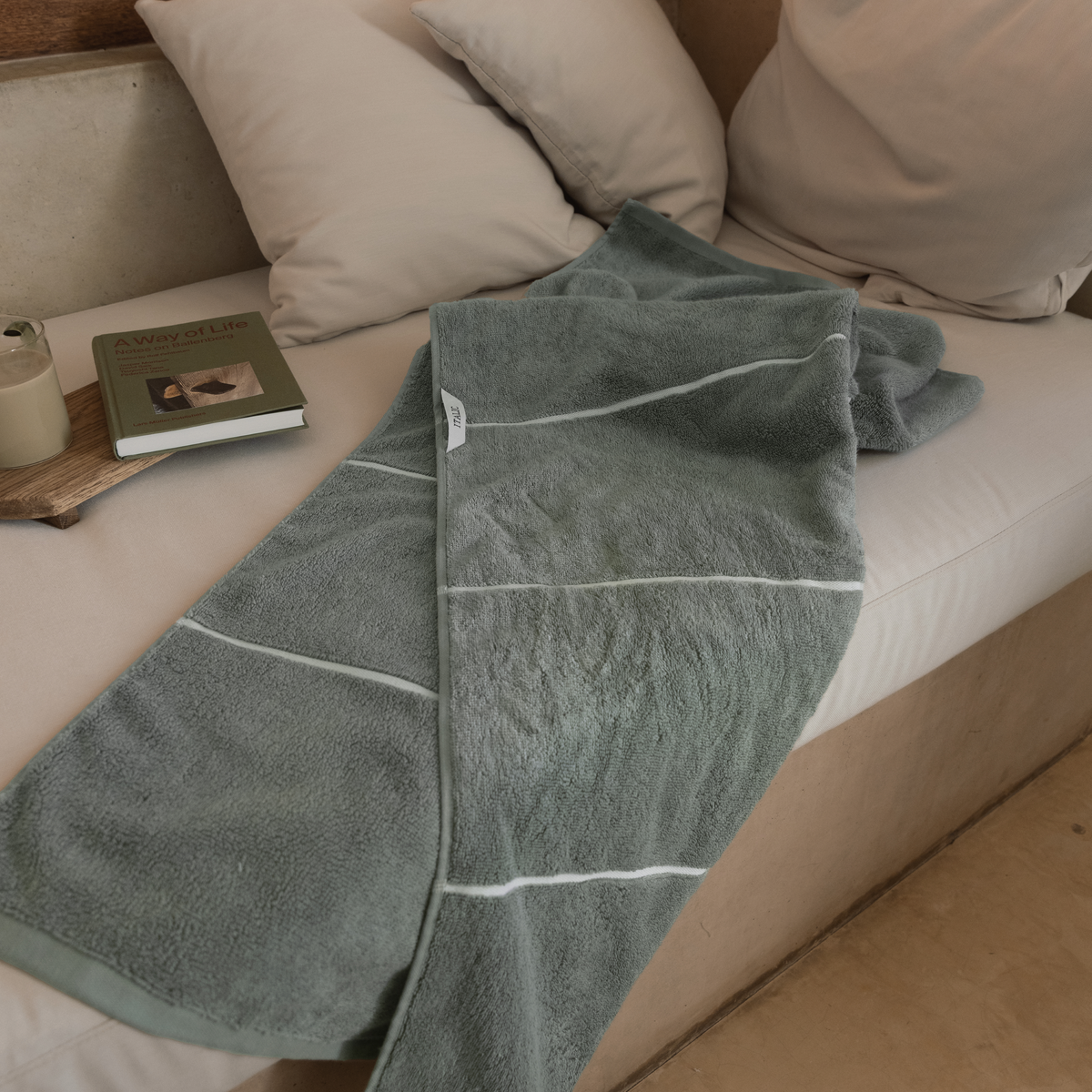 Sage green cotton towel folded on sofa, with white stripe border detail