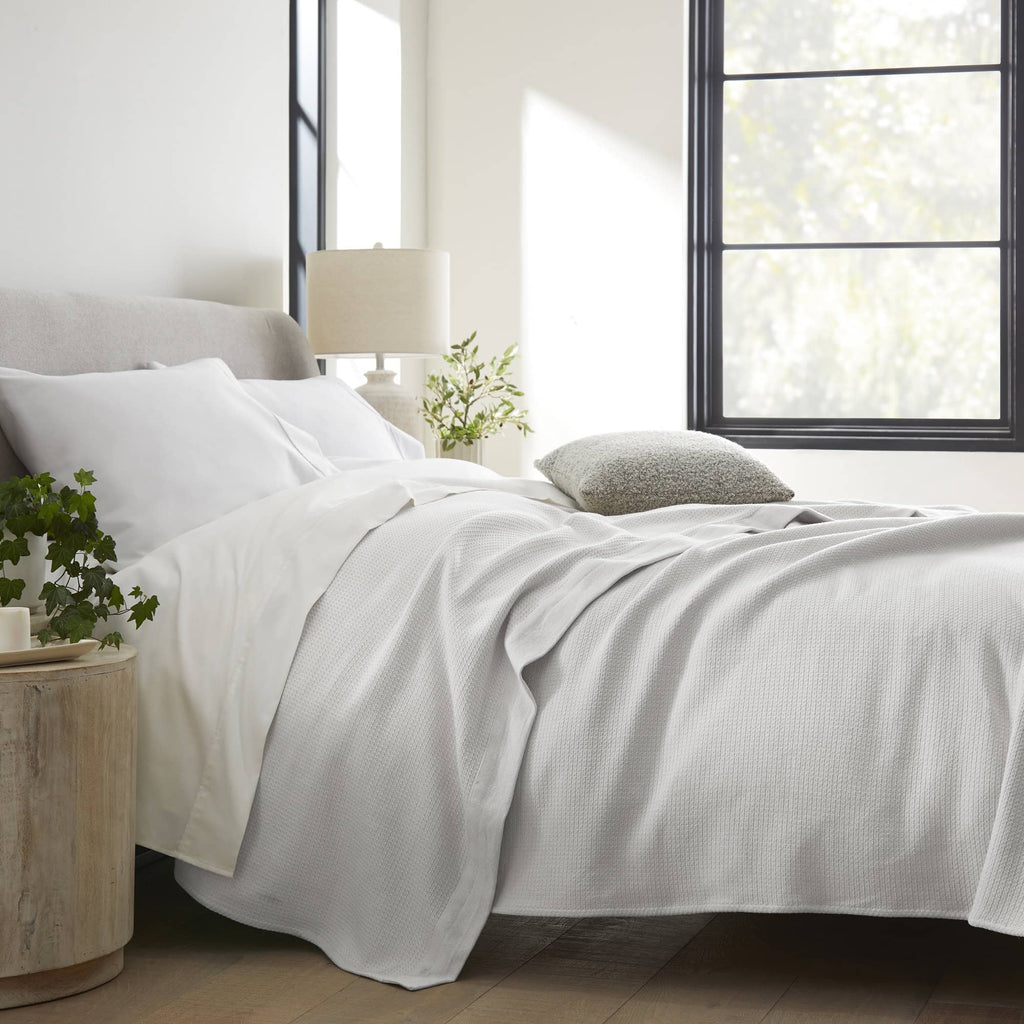 White woven blanket draped across a bed with matching pillows.