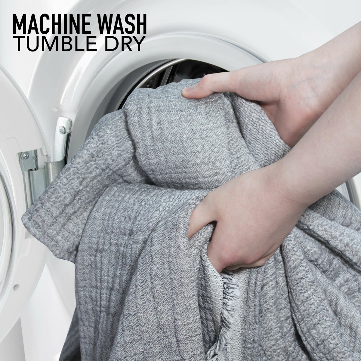 Grey muslin coverlet being placed in a washing machine for machine wash tumble dry