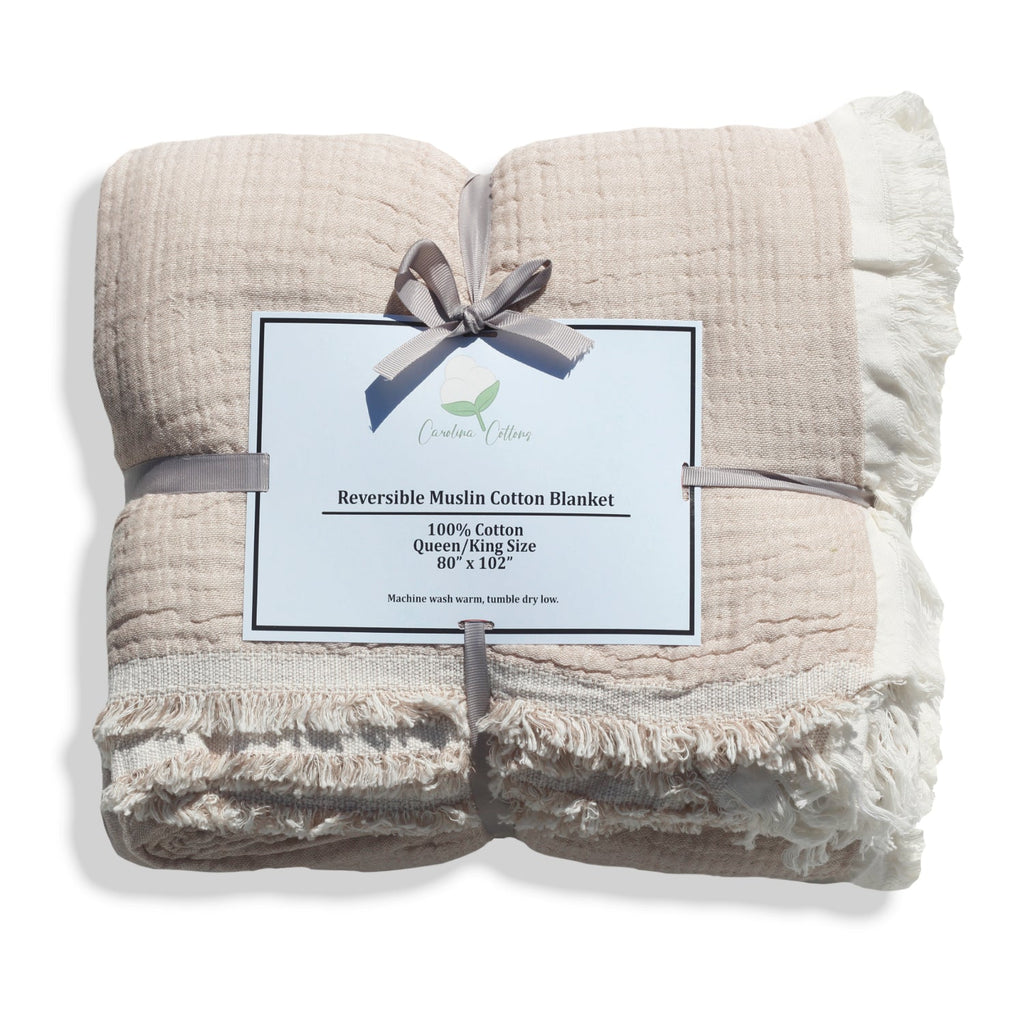 Reversible muslin cotton coverlet folded in light coffee-beige and ivory with fringe