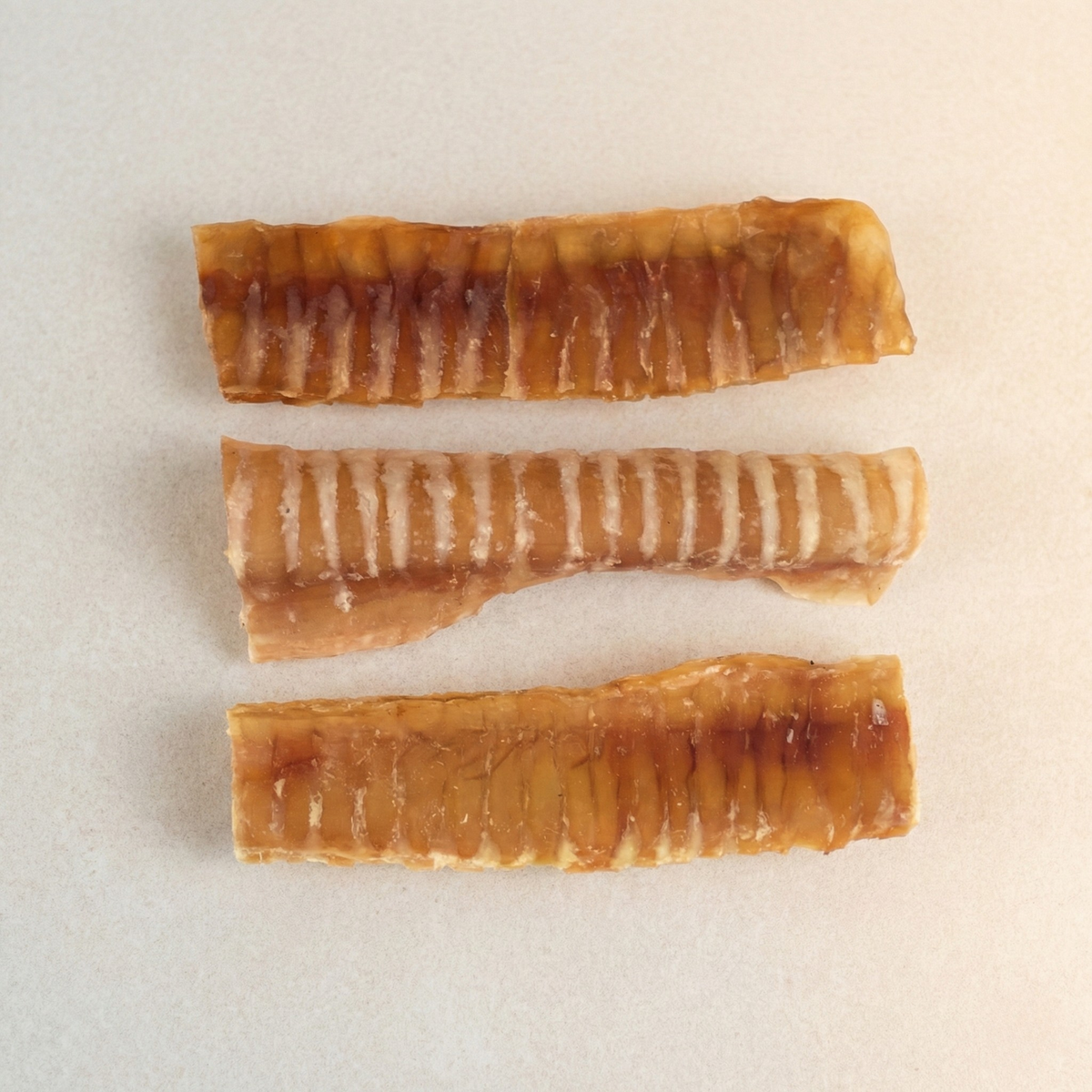 Three beef trachea chew strips on a light surface, ridged and dehydrated