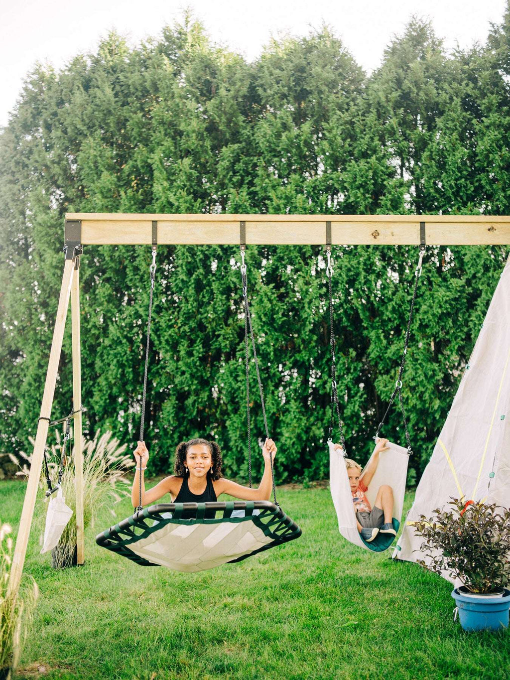Two children’s rope swings on a backyard frame with woven seats and hanging ropes