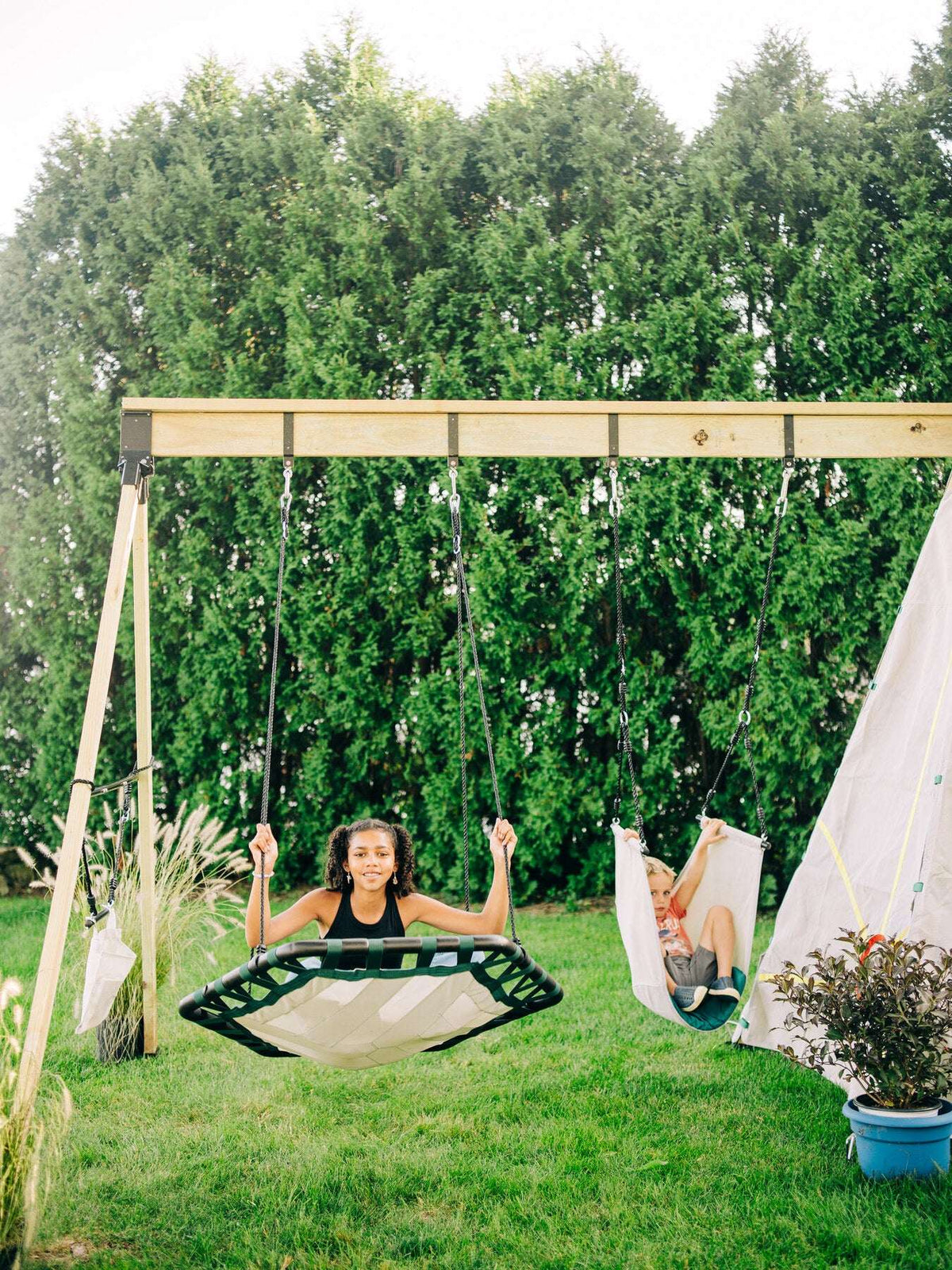Two children’s rope swings on a backyard frame with woven seats and hanging ropes