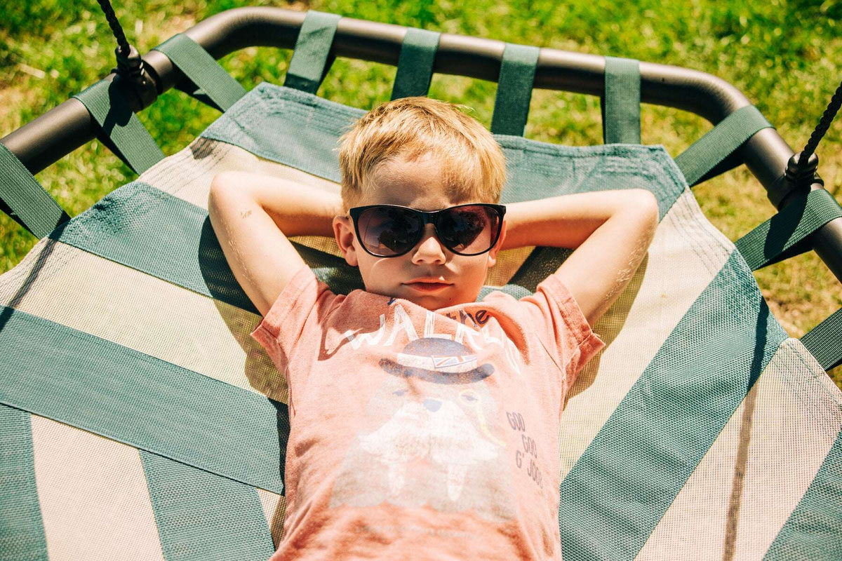 Child seated on a green rope swing with striped fabric seat and hanging ropes