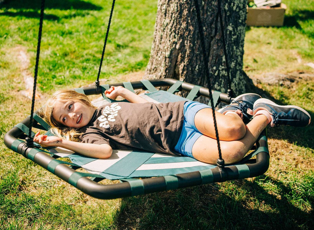 Child lying on a green rope swing with striped woven seat and hanging ropes