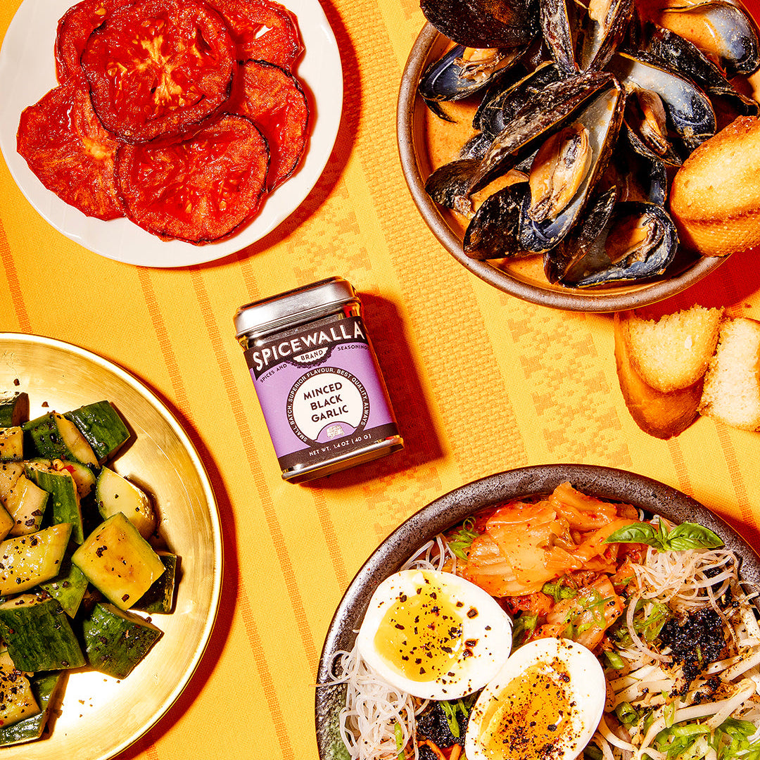 Spicewala minced black garlic seasoning jar with plates of cooked dishes