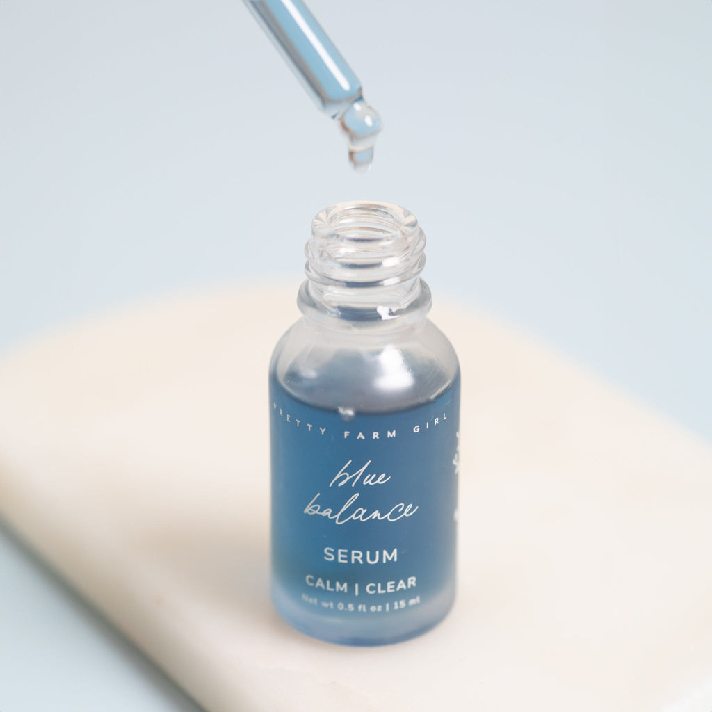 Blue face serum bottle with dropper pouring a clear liquid