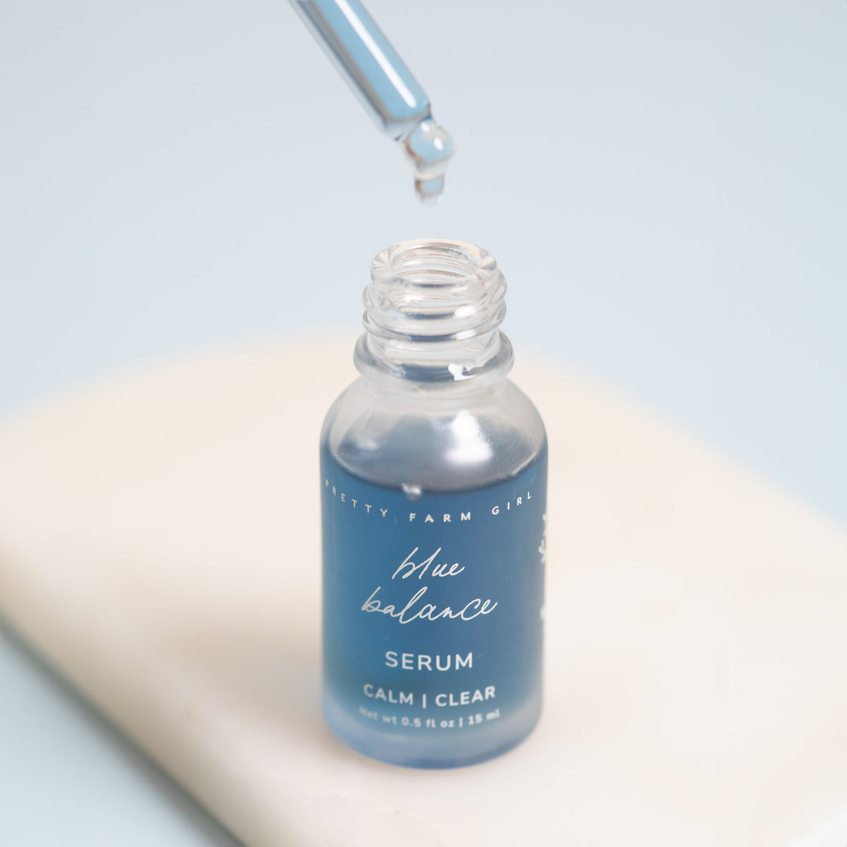Blue face serum bottle with dropper pouring a clear liquid