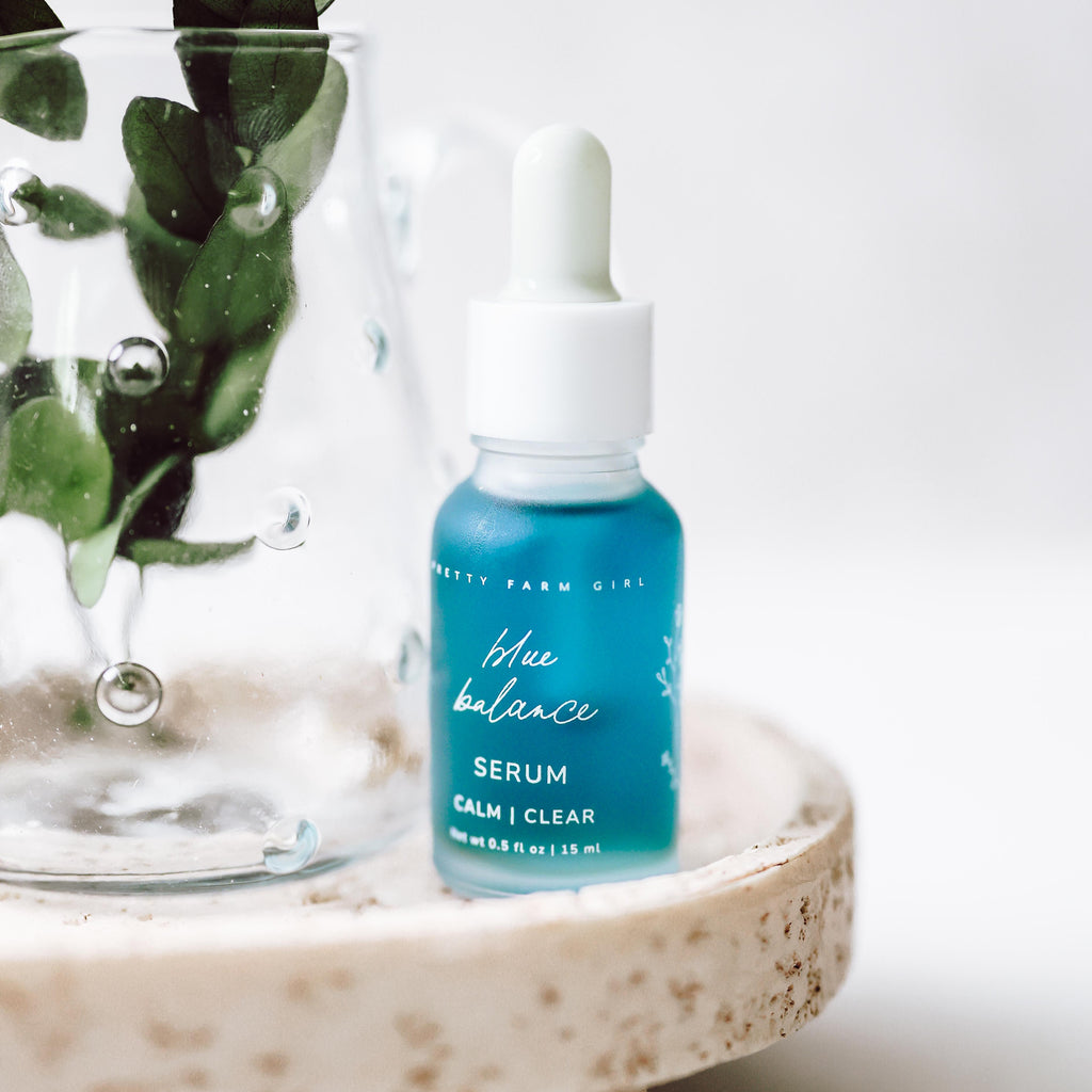 Blue face serum bottle with white dropper cap on stone surface