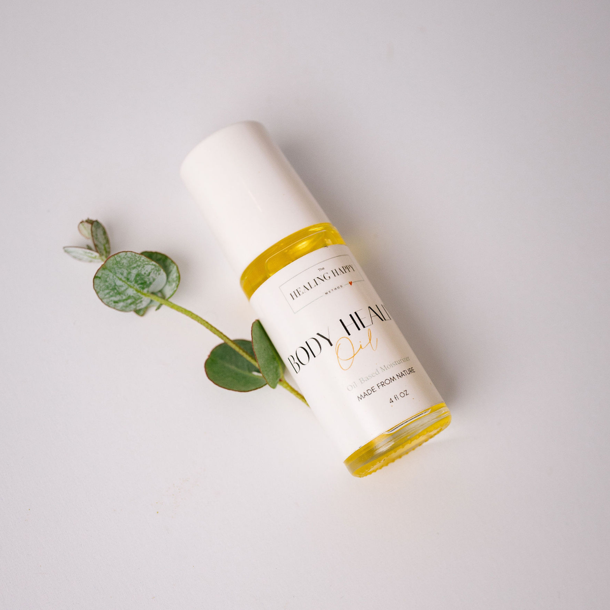 Travel-sized body healing oil bottle with gold cap and label, beside green leaves