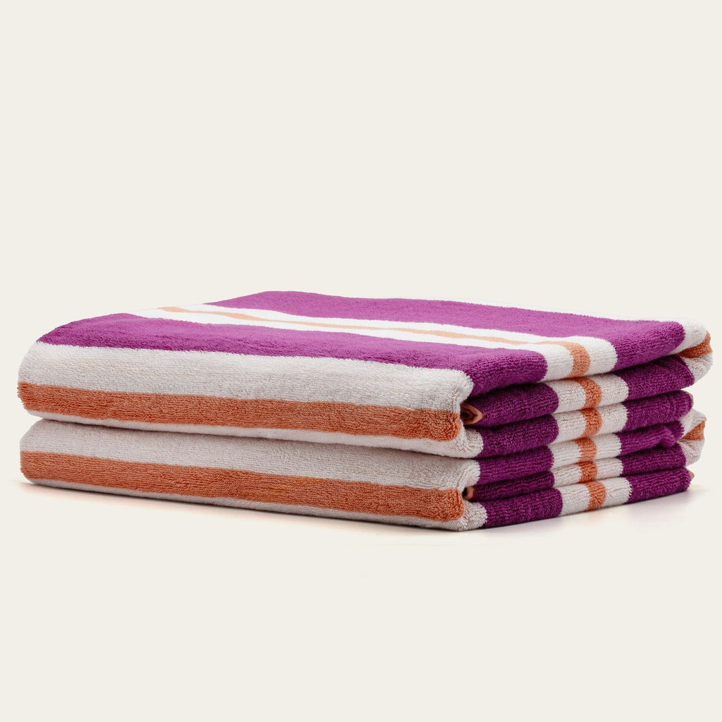 Stack of cotton beach towels with purple and cream stripes and orange edges