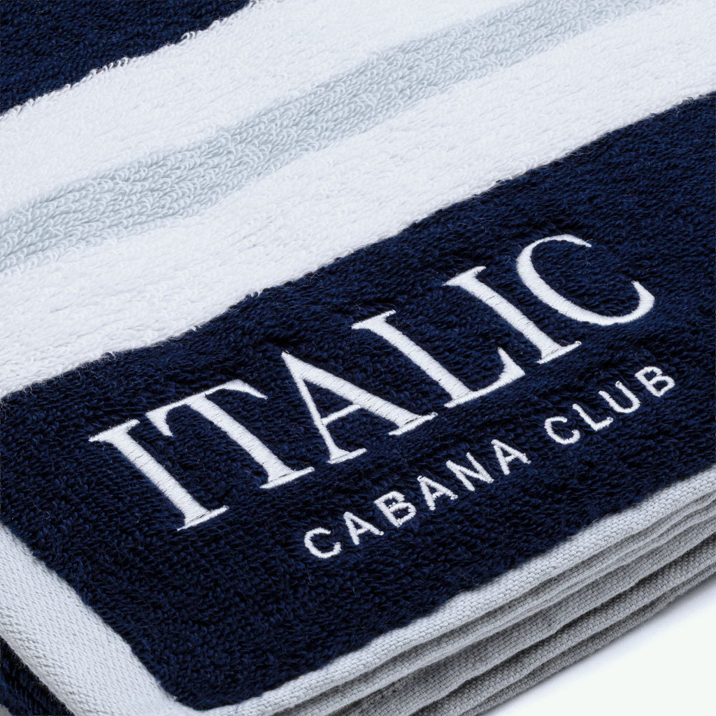 Cotton beach towel close-up of "ITALIC" and "CABANA CLUB" embroidery on navy stripe