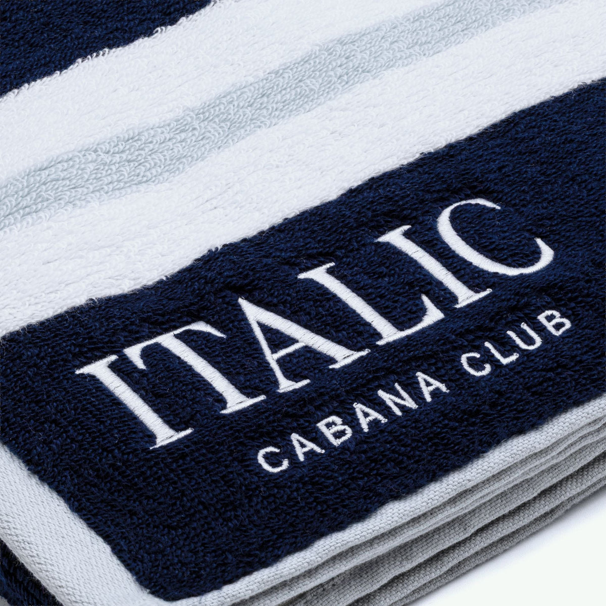 Cotton beach towel close-up of "ITALIC" and "CABANA CLUB" embroidery on navy stripe