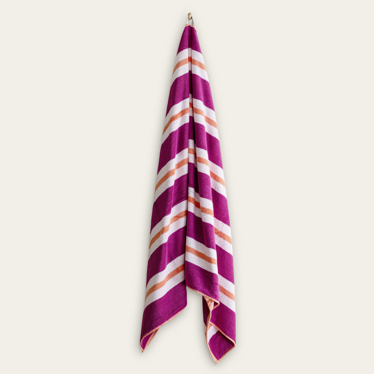 Cotton beach towel with purple and cream diagonal stripes, folded over and hanging