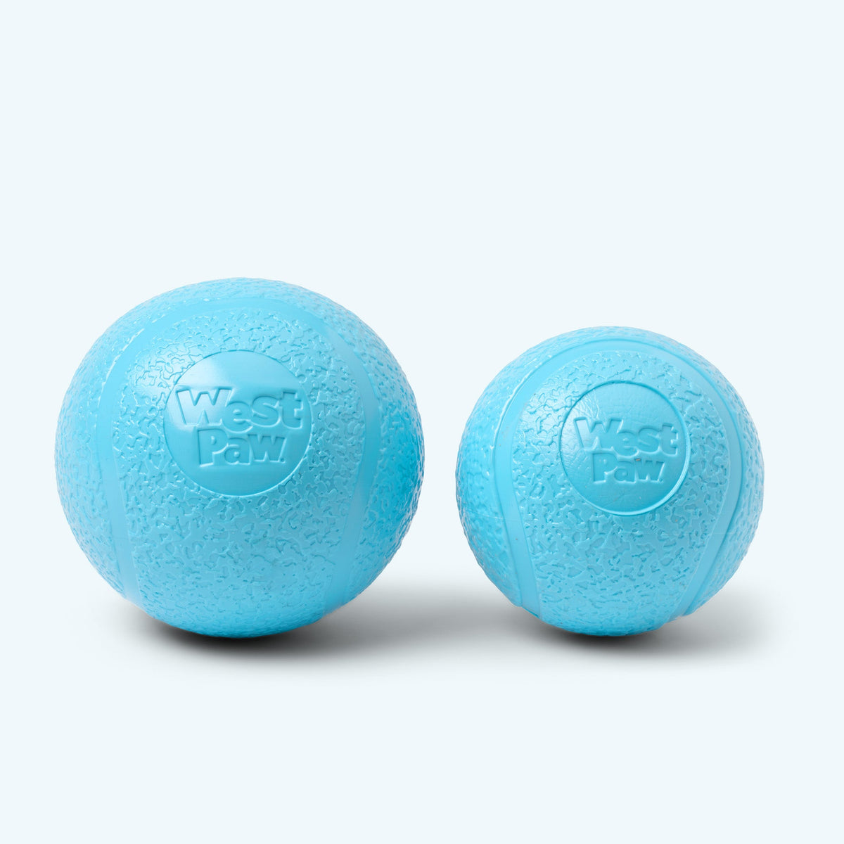 Two light-blue textured dog balls with embossed West Paw logos.