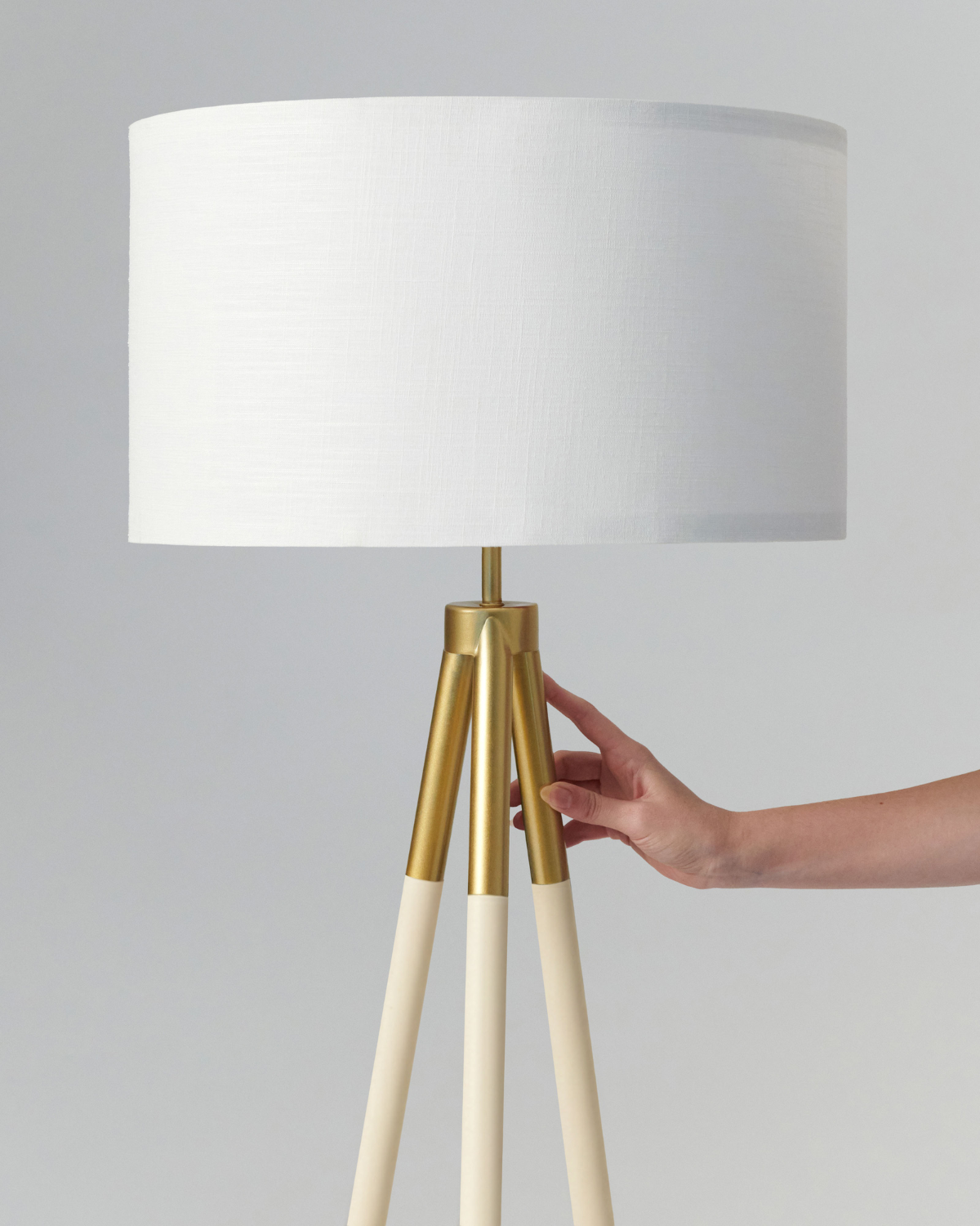 Levi floor lamp close-up: cream fabric shade on gold tripod base and light wood legs