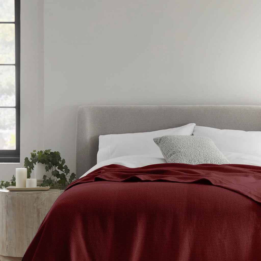 Deep red woven blanket on a bed with a gray pillow.