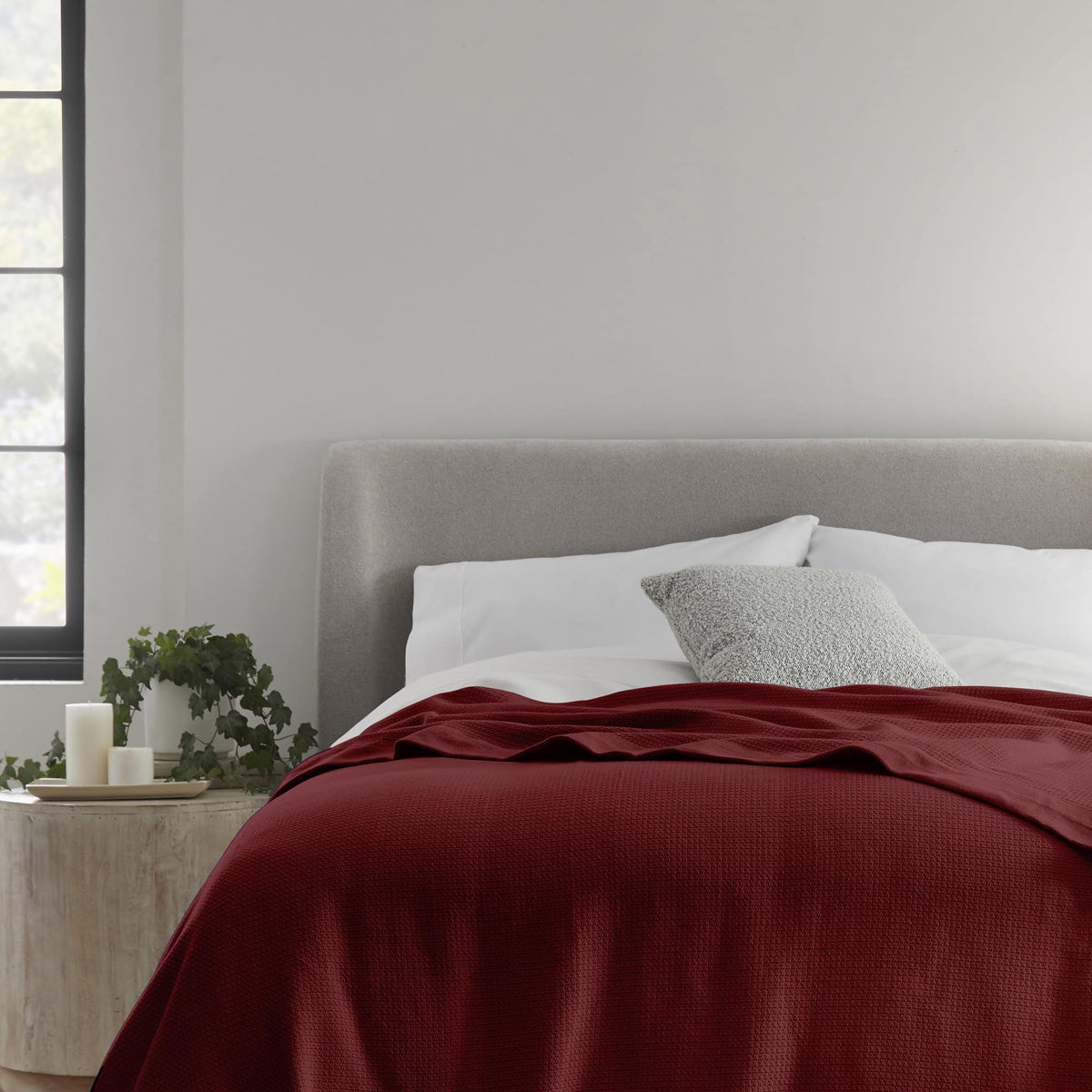 Deep red woven blanket on a bed with a gray pillow.