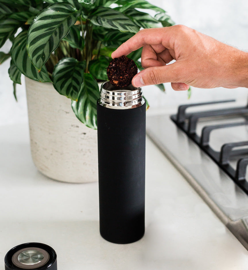 Black tea disc being placed into a cylindrical tea infuser