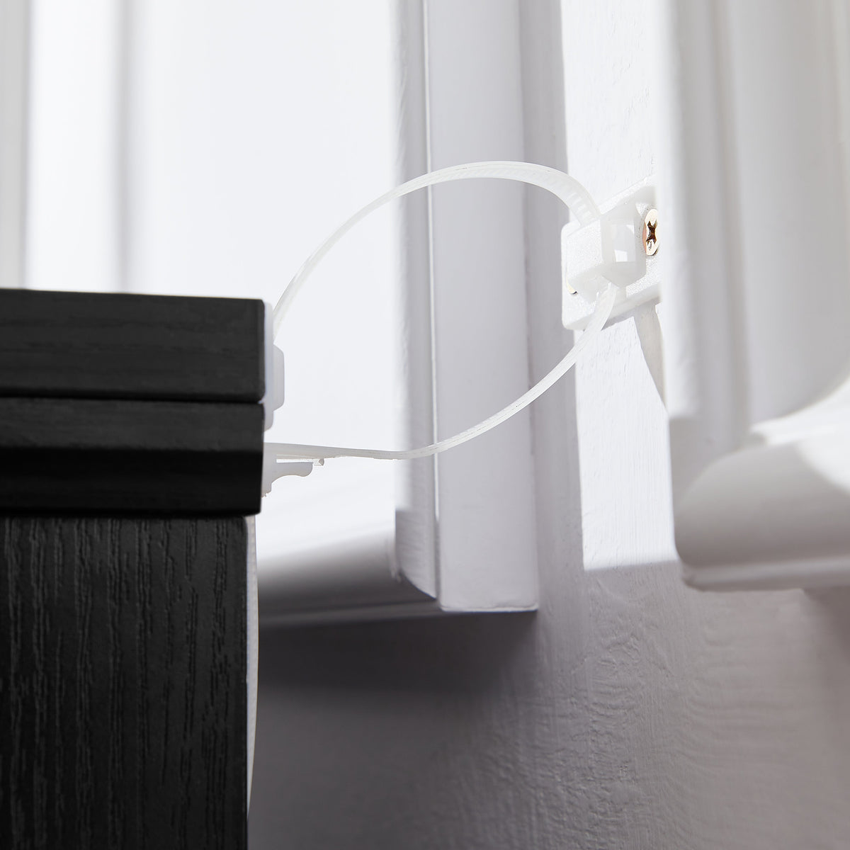 Anti-tipping strap attached to the side of a black chest of drawers
