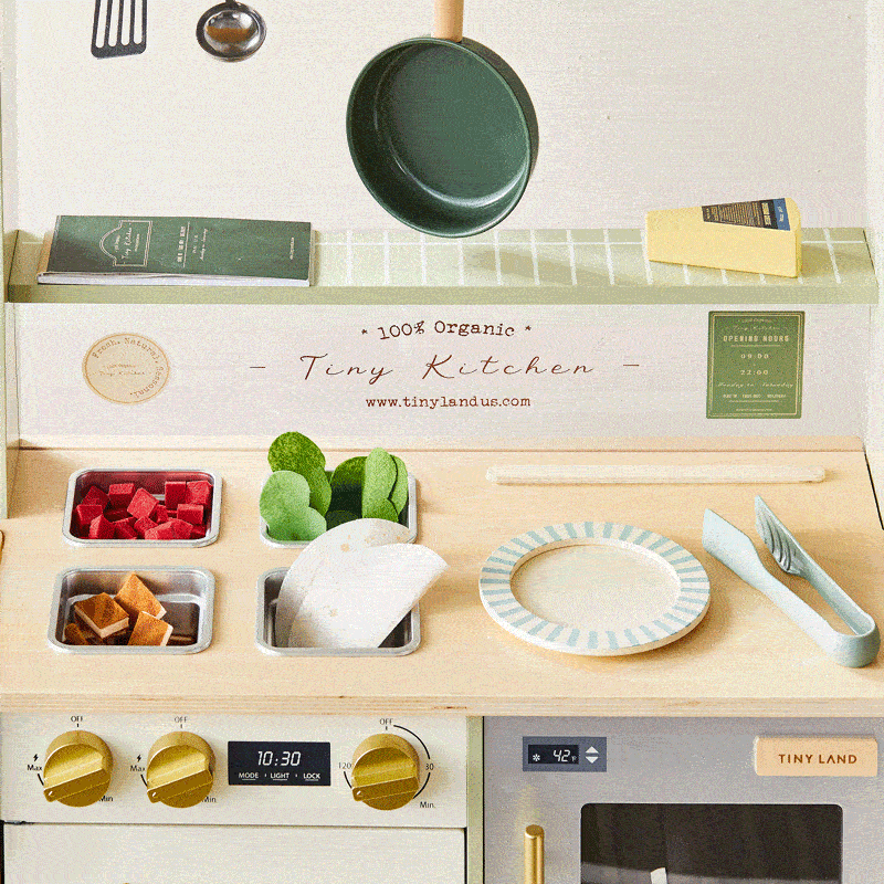 Mini kitchen countertop with cookware, plate, utensils, and small food props.