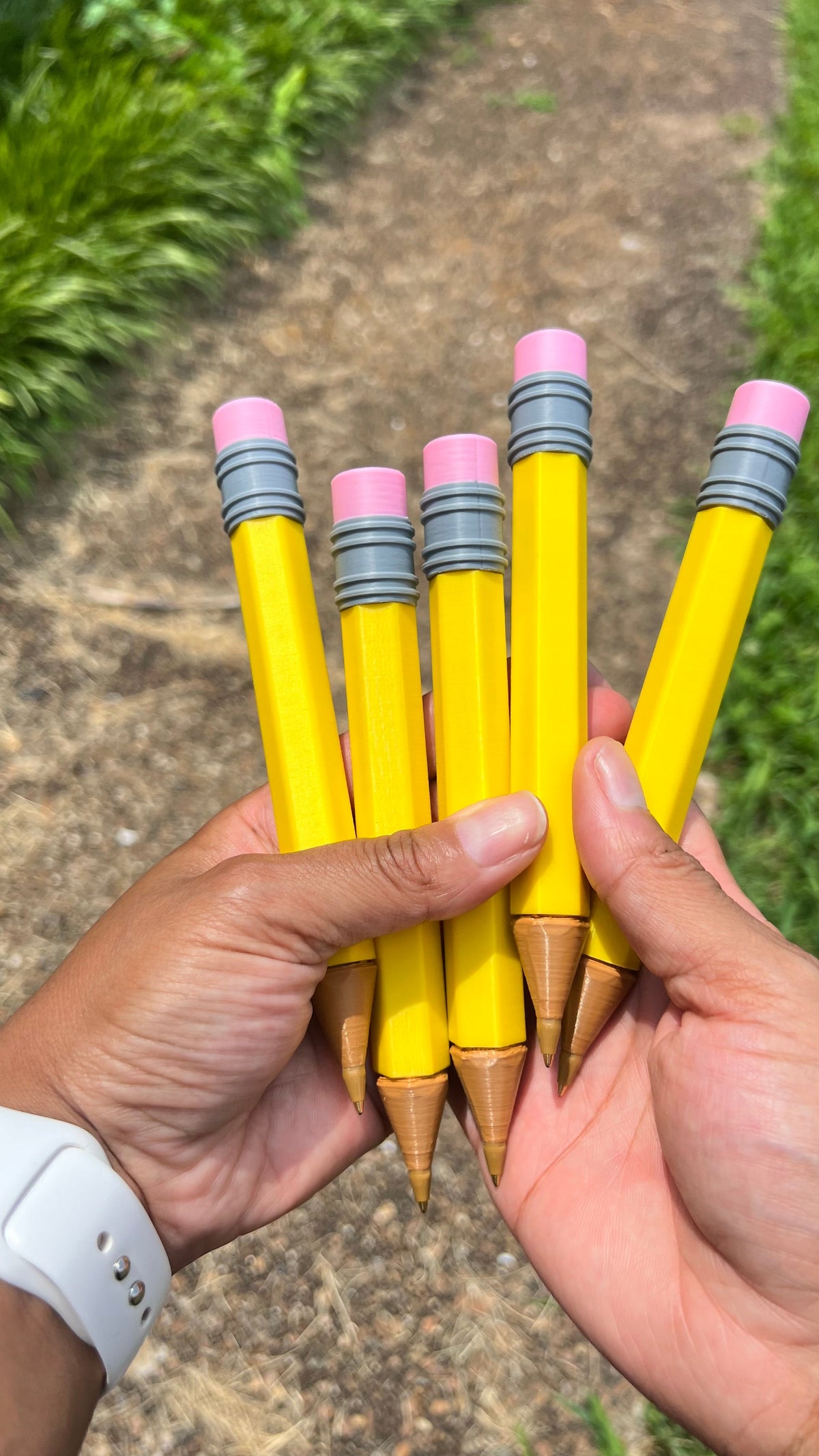 Jumbo yellow novelty pencils held in hands, pink erasers and gray striped grips, wooden tips